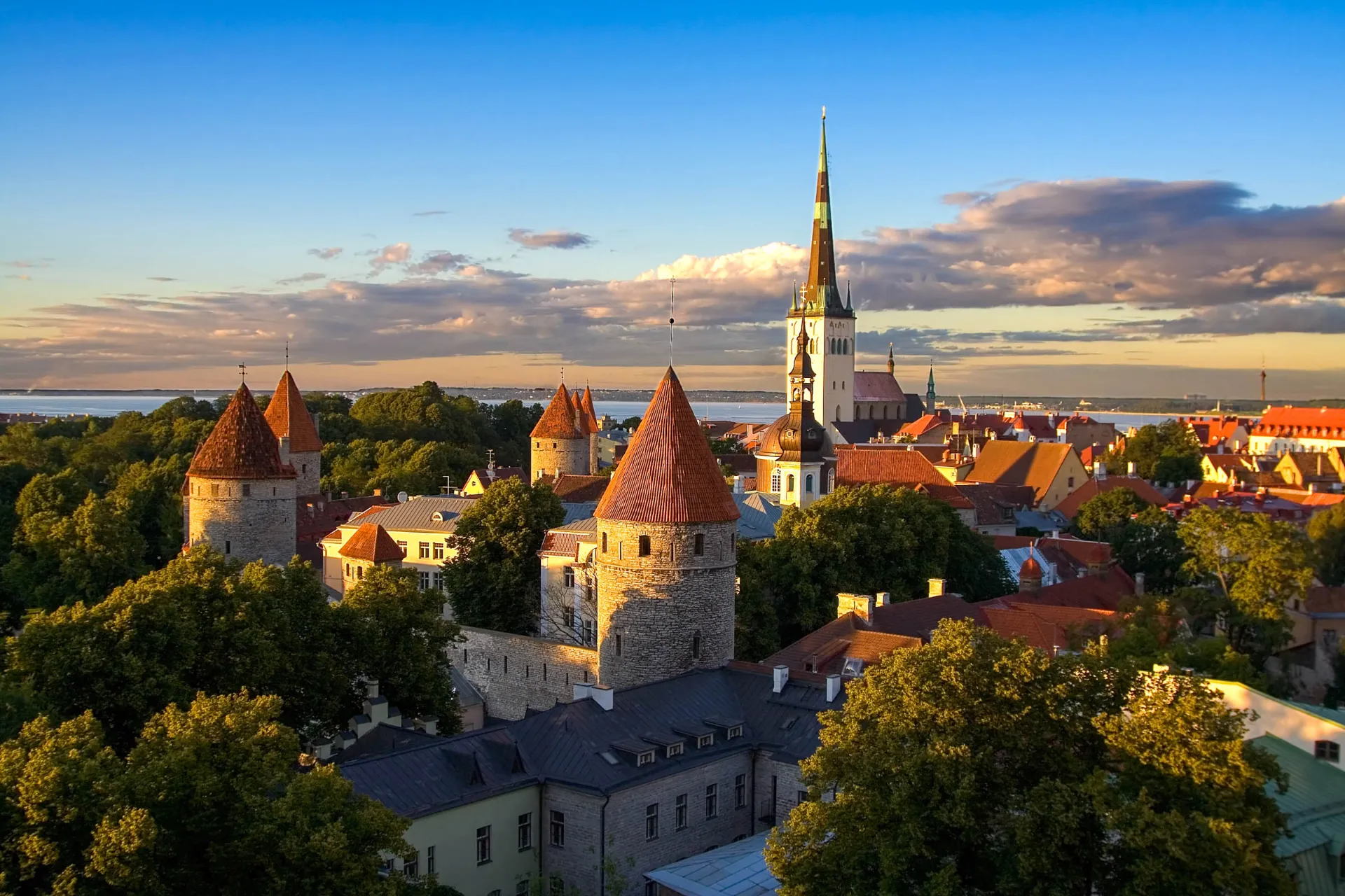 Zachód słońca nad średniowiecznym starym miastem w Tallinnie z murami miejskimi i kościołem św. Olafa w tle Zachód słońca nad średniowiecznym starym miastem w Tallinnie z murami miejskimi i kościołem św. Olafa w tle