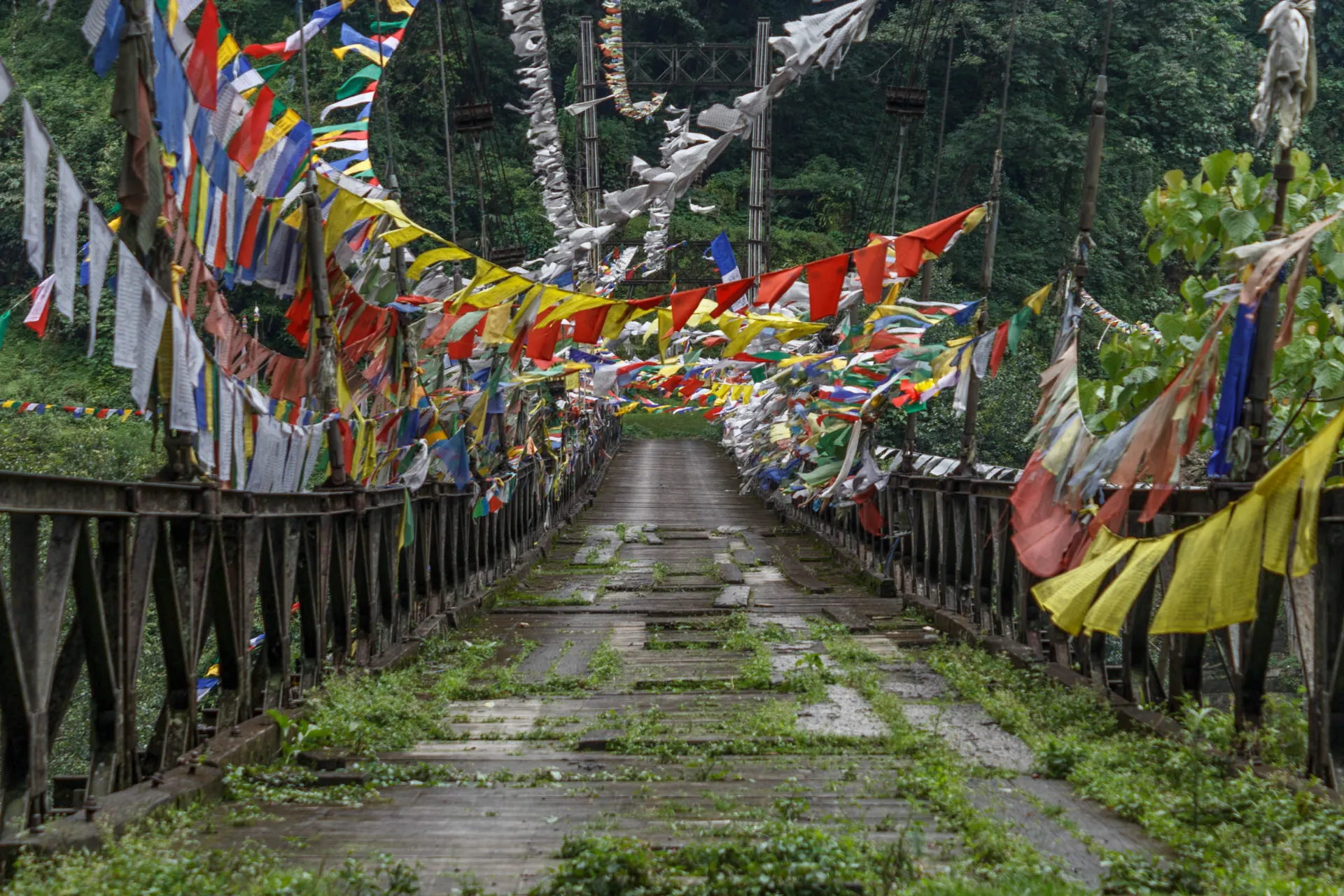 Wiszący most z kolorowymi flagami modlitewnymi - wygląda na trochę zużyty Wiszący most z kolorowymi flagami modlitewnymi - wygląda na trochę zużyty