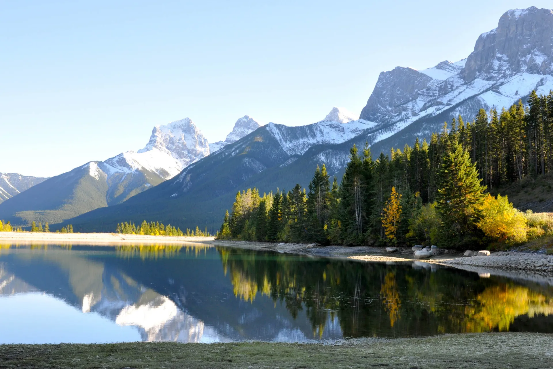 Ośnieżone góry i las odbijają się w spokojnym jeziorze koło Canmore, Alberta Ośnieżone góry i las odbijają się w spokojnym jeziorze koło Canmore, Alberta