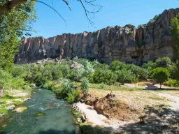 Rzeka w bujnej Dolinie Ihlara ze stromymi ścianami skalnymi w tle pod błękitnym niebem