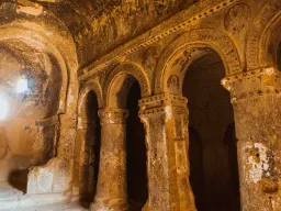 Wnętrze starego kościoła jaskiniowego w Kapadocji, z wyrzeźbionymi kolumnami, łukami i pozostałościami dekoracji w ścianach skalnych