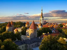 Zachód słońca nad średniowiecznym starym miastem w Tallinnie z murami miejskimi i kościołem św. Olafa w tle Zachód słońca nad średniowiecznym starym miastem w Tallinnie z murami miejskimi i kościołem św. Olafa w tle