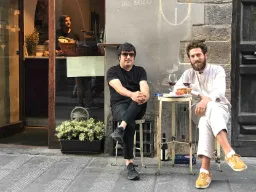 Dwaj mężczyźni piją wino przy małym stoliku na ulicy