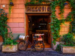Klimatyczna ulica w rzymskiej dzielnicy Trastevere z wejściem do klasycznej włoskiej pizzerii Klimatyczna ulica w rzymskiej dzielnicy Trastevere z wejściem do klasycznej włoskiej pizzerii