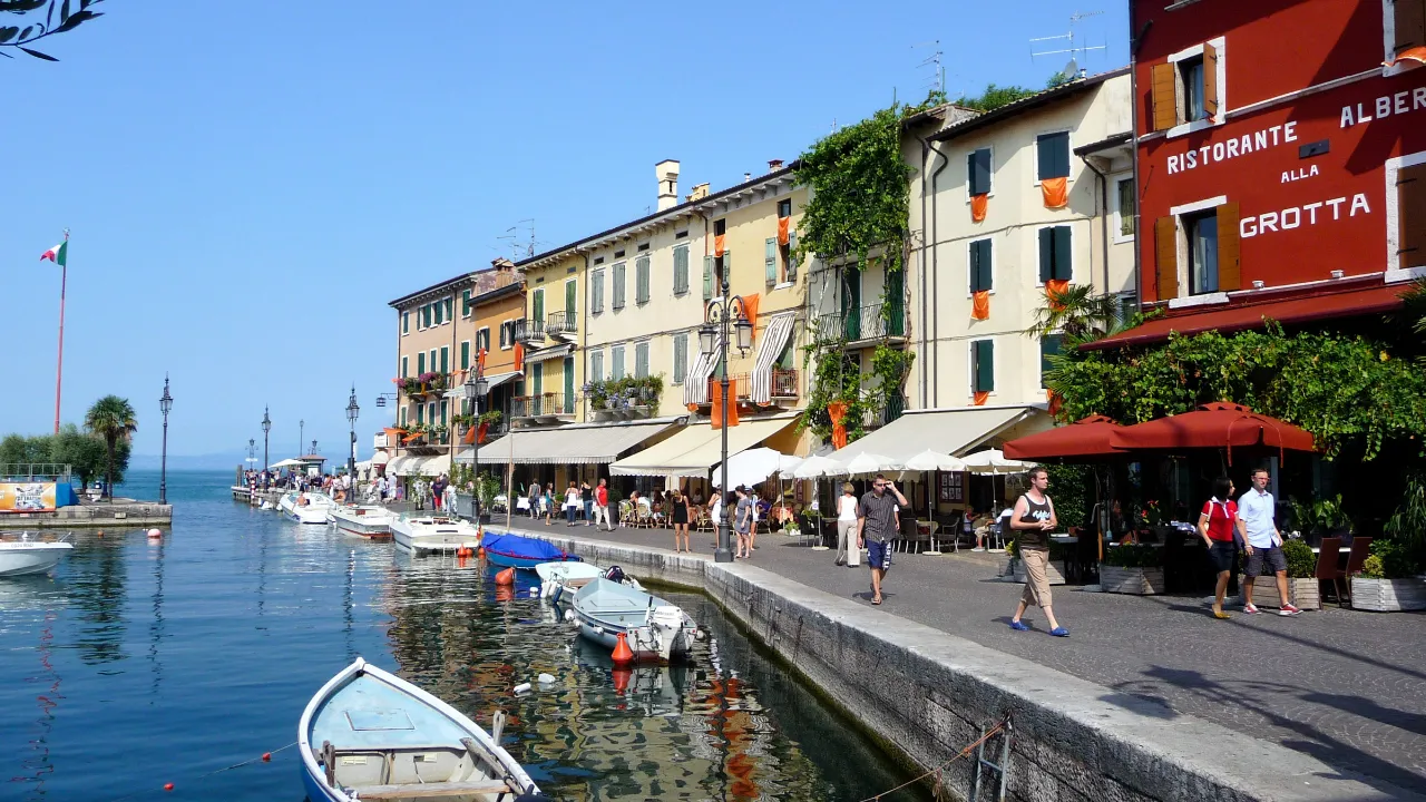 Port w Lazise nad jeziorem Garda z łodziami, promenadą i zabytkowymi budynkami nad wodą